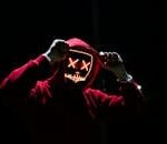 A spooky illuminated mask figure with a red hoodie in a dark setting, perfect for Halloween themes.